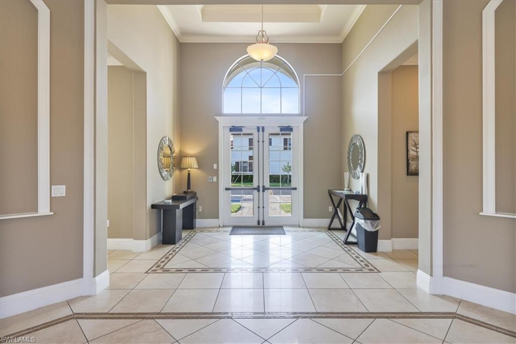 Tiled foyer entrance with crown molding, french doors, baseboards, a raised ceiling, and a high ceiling