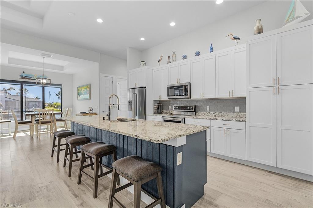 Kitchen with appliances with stainless steel finishes, sink, an island with sink, white cabinets, and light tile flooring