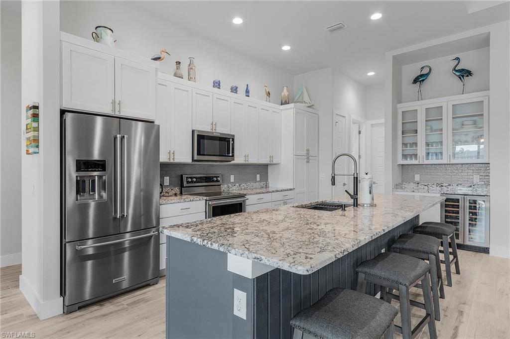Kitchen with wine cooler, white cabinets, an island with sink, sink, and stainless steel appliances