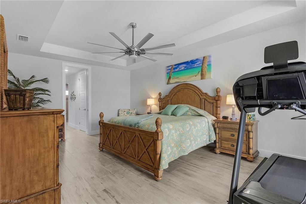 Bedroom featuring ceiling fan, a raised ceiling, and light tile floors