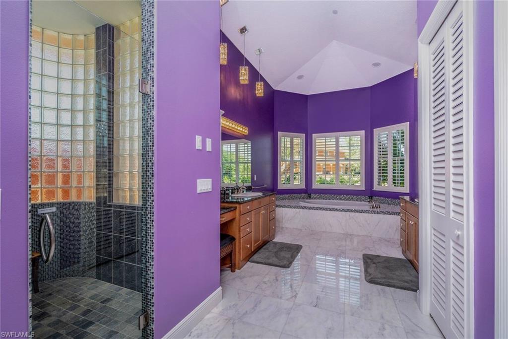 Master Bathroom downstairs with linen closet, dual vanities & sinks, jetted tub, rain shower, private toilet room, marble  flooring, and high vaulted ceiling