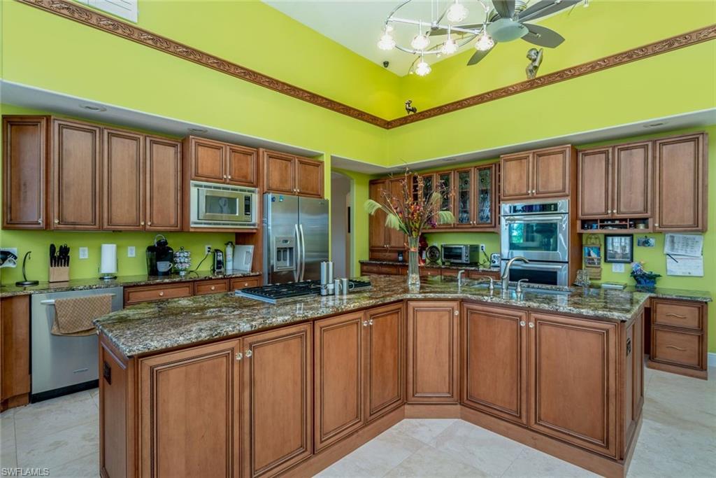 Kitchen with appliances with stainless steel finishes, med brown Brookwood cabinetry, high counters, and granite countertops, high ceiling