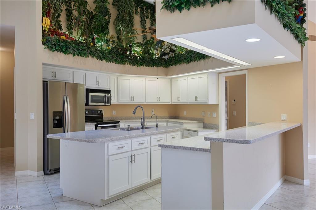 Kitchen with stainless steel appliances, high vaulted ceiling, light tile patterned floors, light countertops, and a chandelier