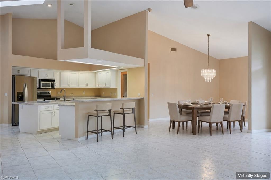 Kitchen featuring stainless steel dishwasher, a sink, a center island with sink, a skylight, and light tile patterned flooring