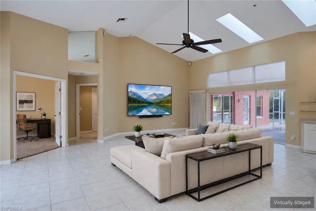 Unfurnished living room featuring high vaulted ceiling, light tile patterned floors, ceiling fan, baseboards, and a skylight