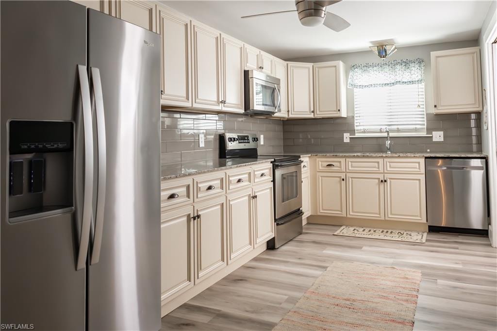 Kitchen with stainless steel appliances, a sink, a ceiling fan, light stone counters