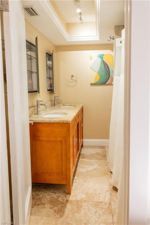 Full bath featuring a raised ceiling, double vanity, and baseboards