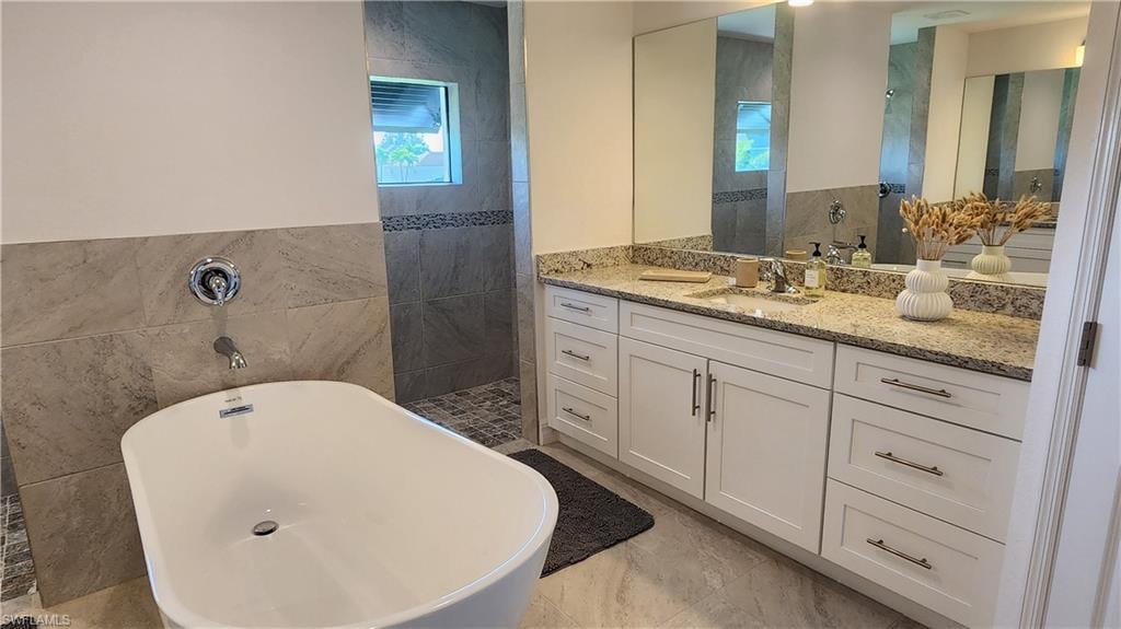 Full bath with tile walls, a freestanding tub, vanity, and a walk in shower
