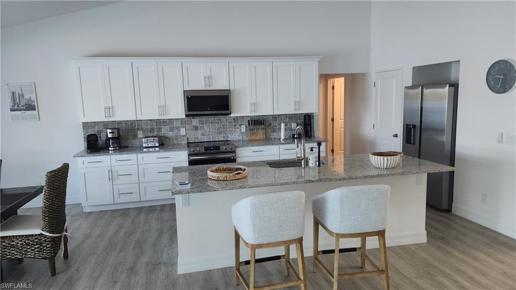 Kitchen featuring appliances with stainless steel finishes, a sink, light wood-style floors, backsplash, and white cabinetry
