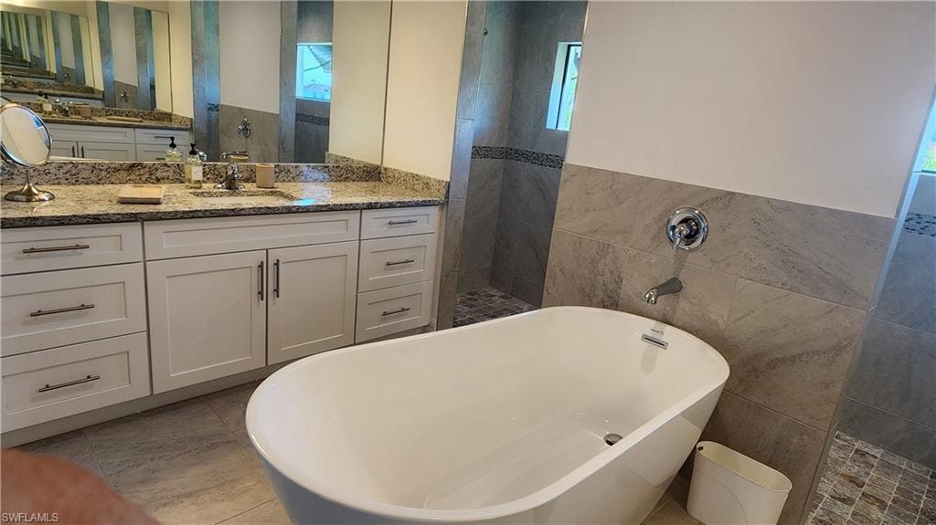 Bathroom featuring tile walls, walk in shower, a freestanding bath, vanity, and a wainscoted wall