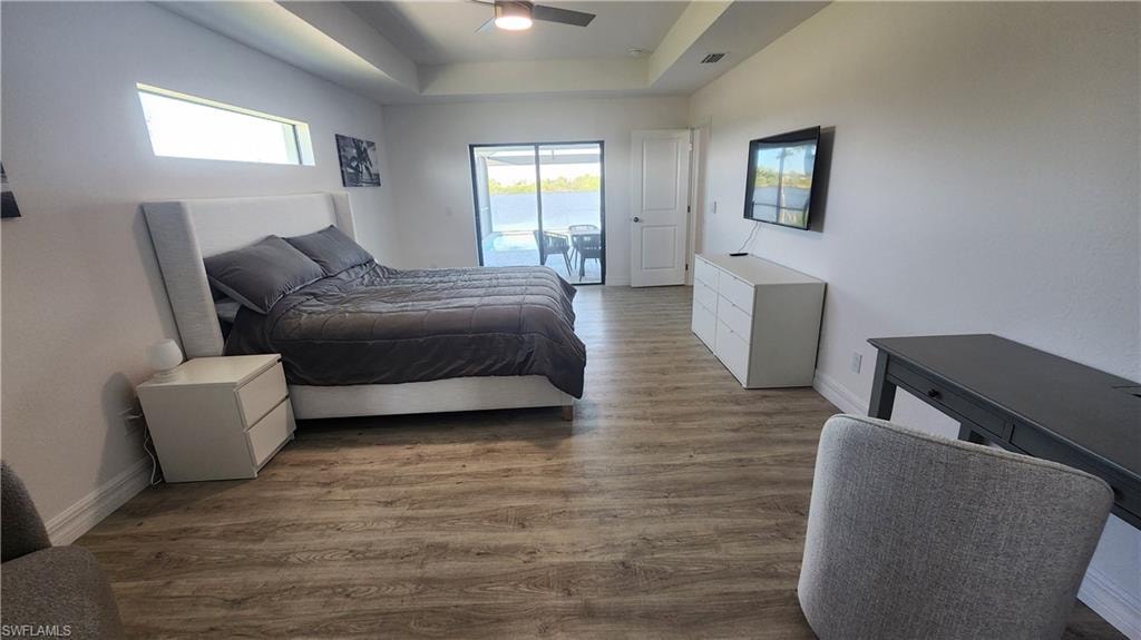 Bedroom with access to exterior, wood finished floors, a raised ceiling, and baseboards