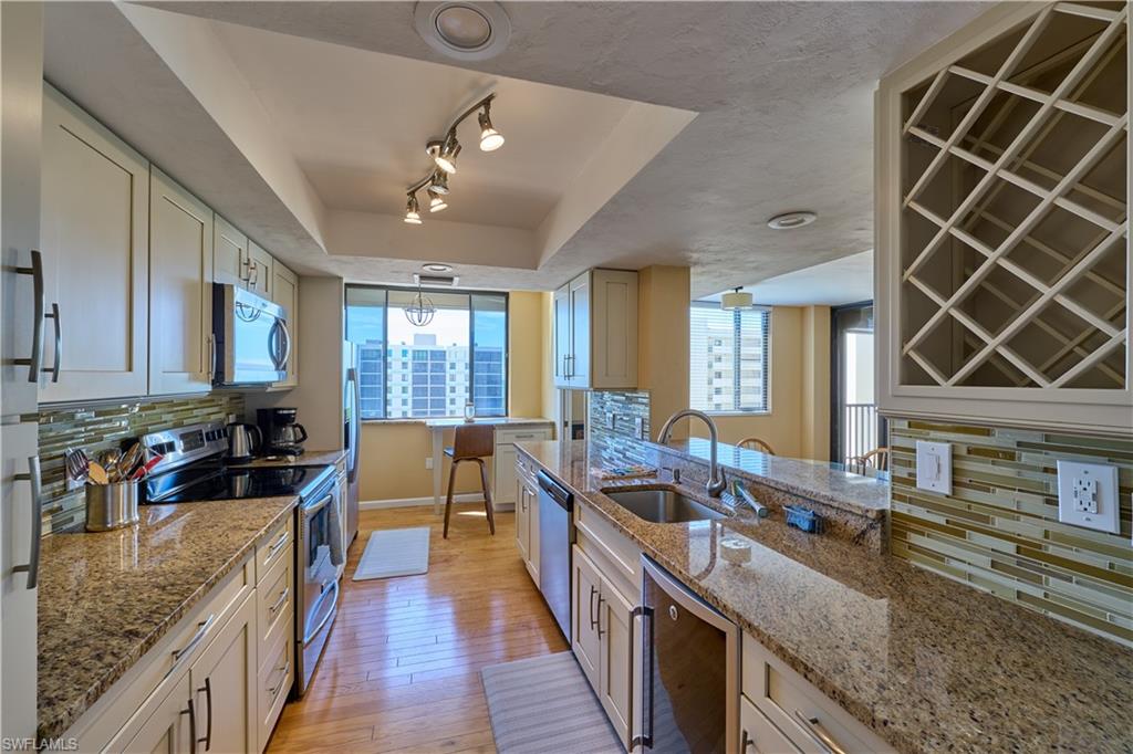 Kitchen featuring backsplash, stainless steel appliances, a raised ceiling, light stone countertops, and light wood finished floors