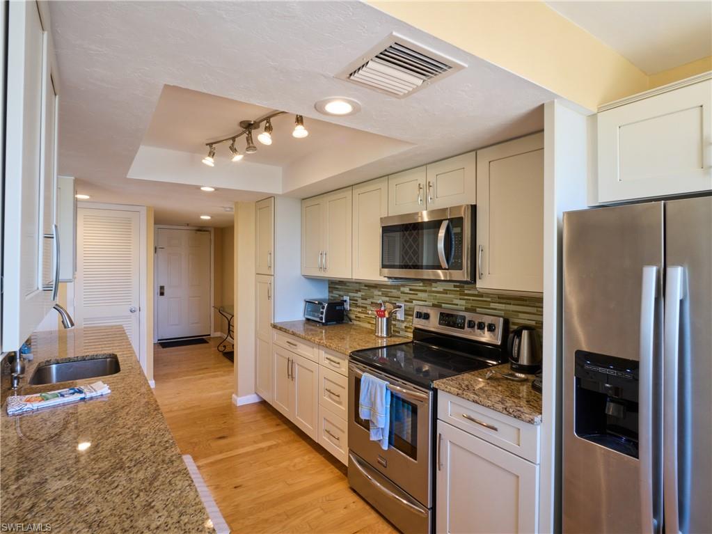 Kitchen with appliances with stainless steel finishes, a sink, a raised ceiling, light wood finished floors, and decorative backsplash