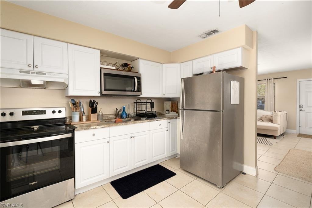 Kitchen with appliances with stainless steel finishes, under cabinet range hood, white cabinets, light tile patterned floors, and a ceiling fan