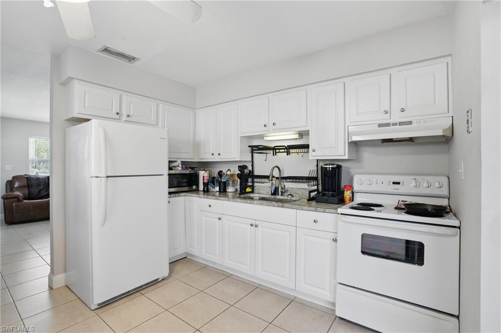 Kitchen with white appliances, under cabinet range hood, a sink, light tile patterned flooring, and white cabinetry