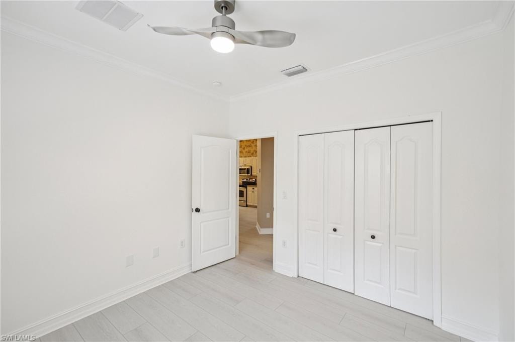 Unfurnished bedroom with crown molding, a closet, light wood-type flooring, and a ceiling fan