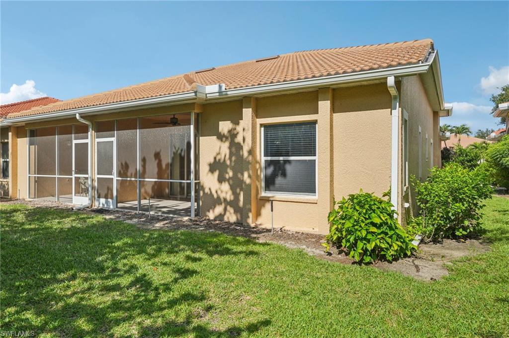 Back of property with a tiled roof, stucco siding, a lawn, and a sunroom