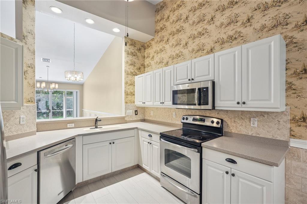 Kitchen featuring wallpapered walls, stainless steel appliances, a chandelier, white cabinetry, and light countertops