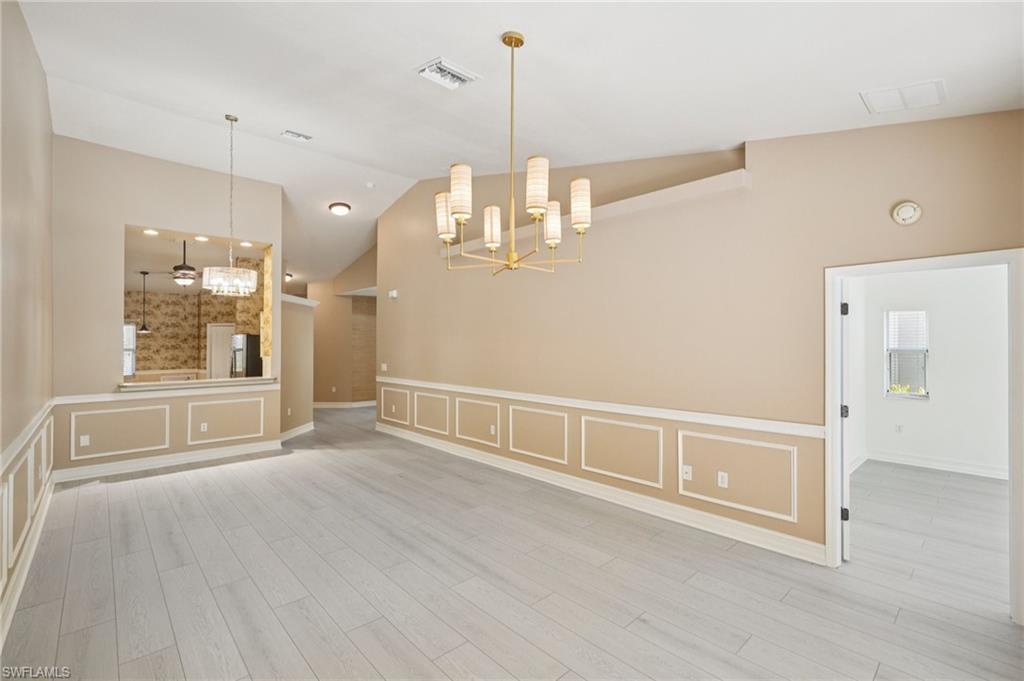 Unfurnished living room featuring a chandelier, lofted ceiling, a decorative wall, wood finished floors, and a wainscoted wall