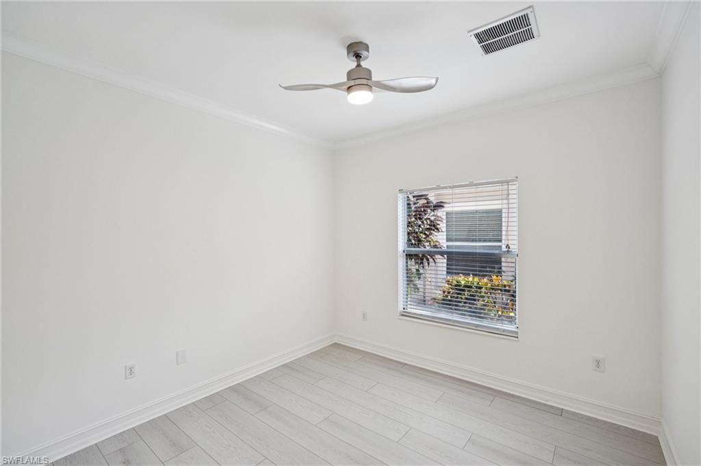Empty room with ornamental molding, ceiling fan, and light wood-style floors