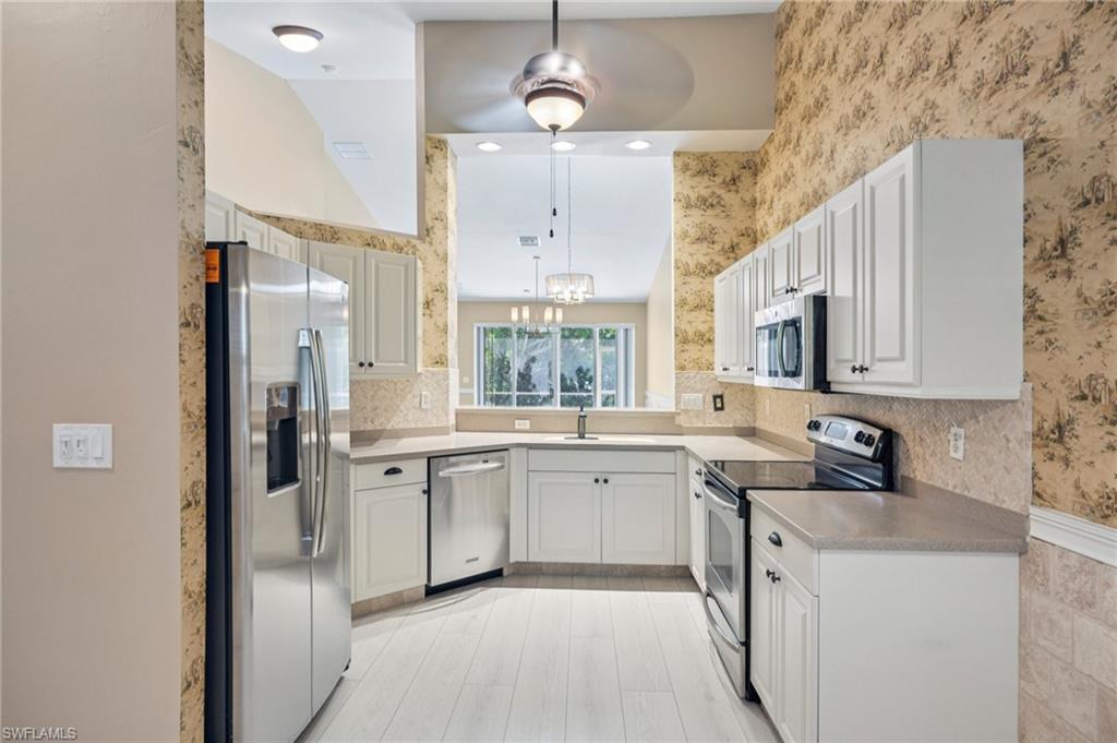 Kitchen featuring appliances with stainless steel finishes, a chandelier, light countertops, wallpapered walls, and decorative light fixtures