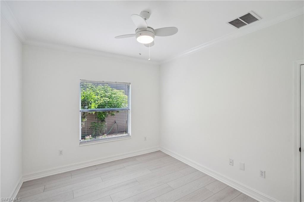Empty room with ornamental molding, ceiling fan, and light wood-style floors