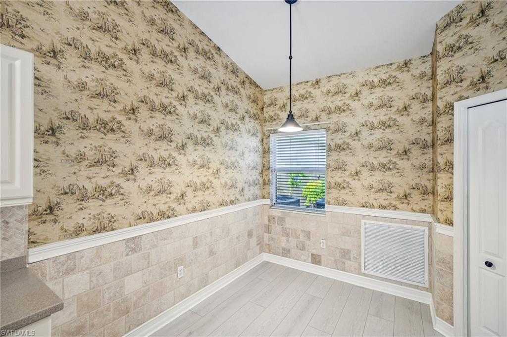 Unfurnished dining area featuring a wainscoted wall, wallpapered walls, and wood finished floors