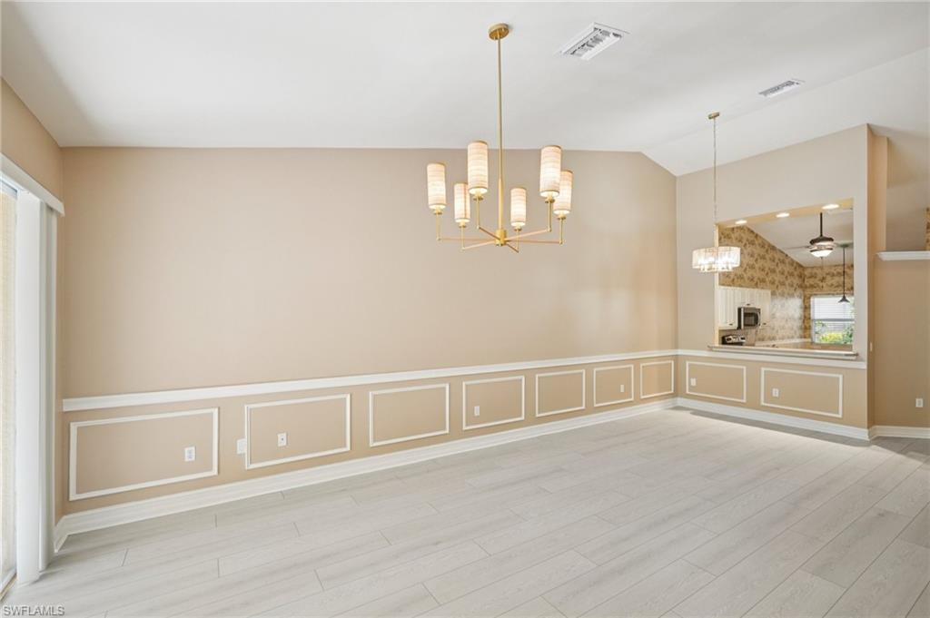 Unfurnished dining area featuring a chandelier, light wood finished floors, a decorative wall, lofted ceiling, and wainscoting