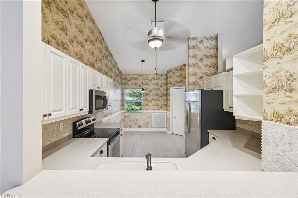 Kitchen featuring vaulted ceiling, wallpapered walls, open shelves, appliances with stainless steel finishes, and ceiling fan