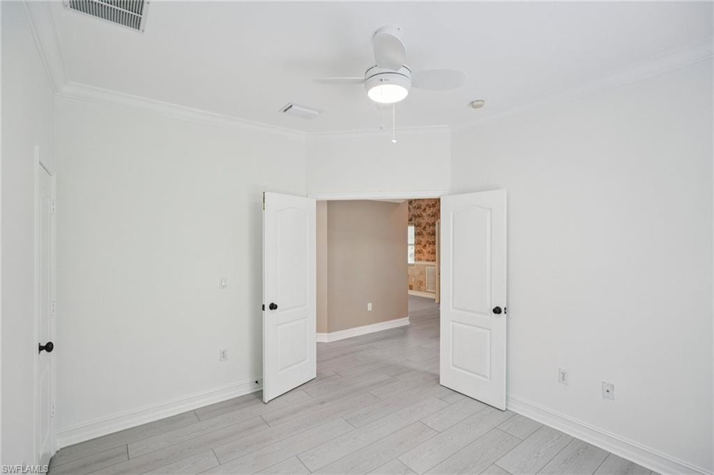 Spare room with ceiling fan, ornamental molding, and light wood-style floors
