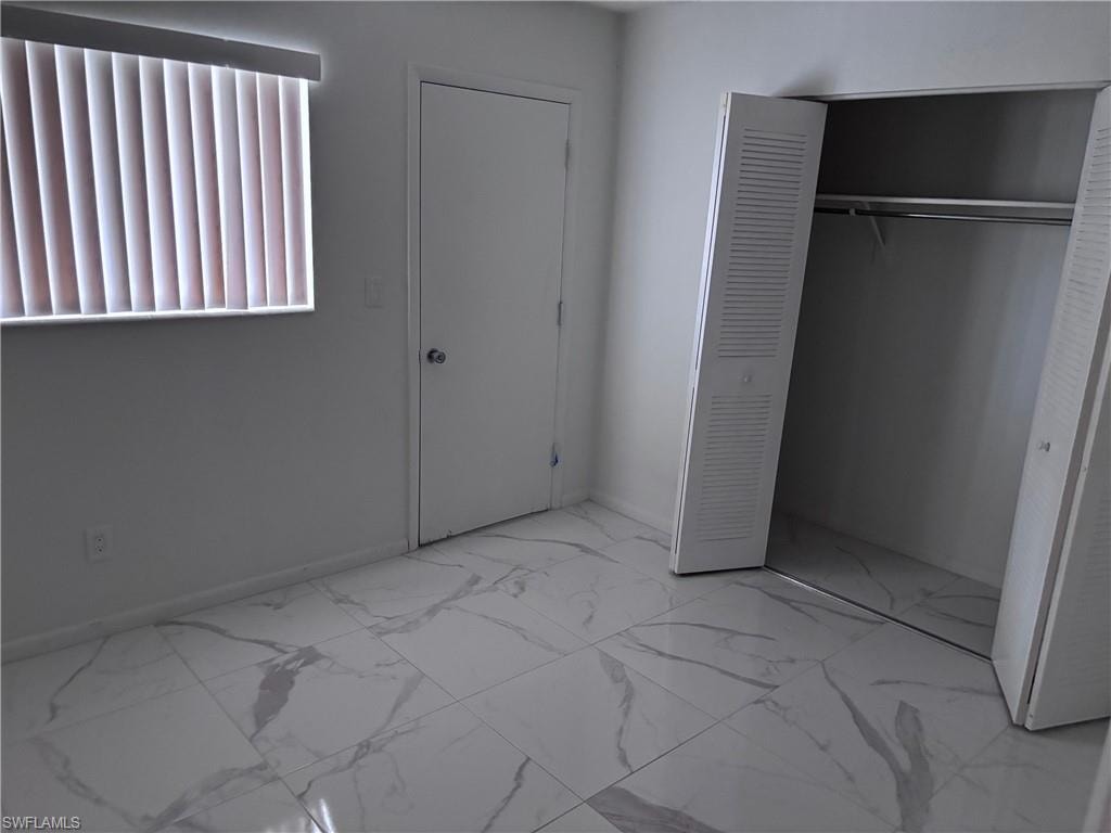 Unfurnished bedroom featuring marble finish flooring, a closet, and baseboards