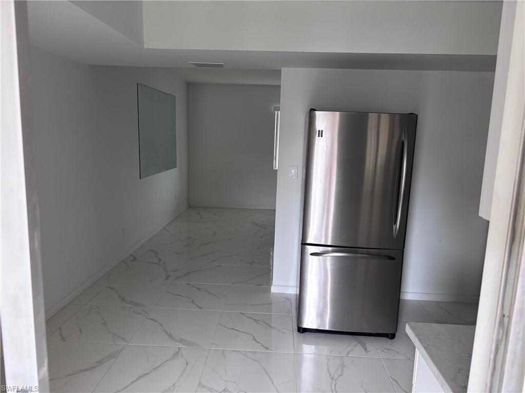 Kitchen with freestanding refrigerator, light marble finish floors, and baseboards