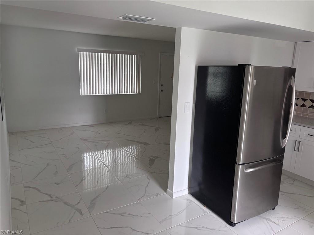 Kitchen with freestanding refrigerator, light marble finish floors, white cabinets, and baseboards