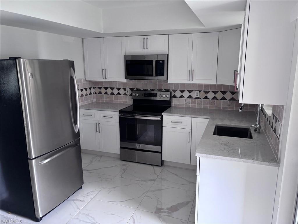 Kitchen with stainless steel appliances, a sink, light marble finish flooring, and white cabinets