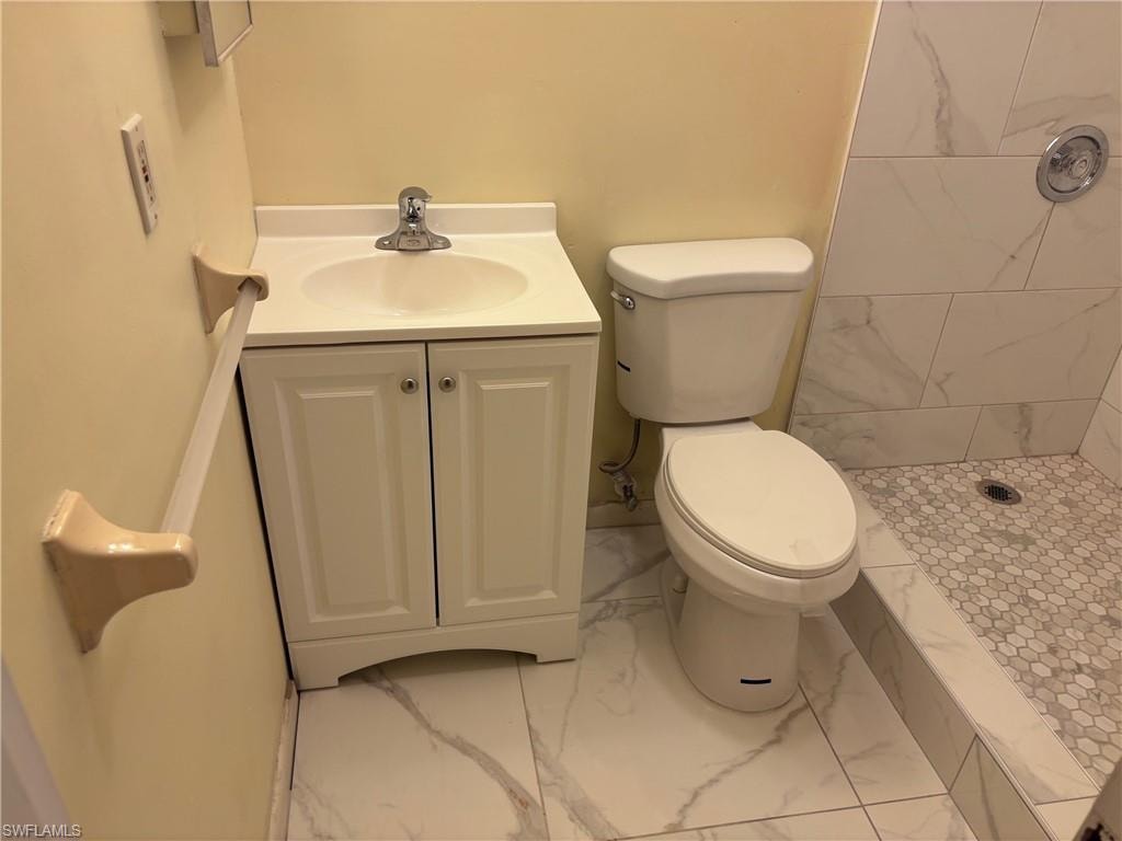 Full bath with marble look tile flooring, a tile shower, toilet, and vanity