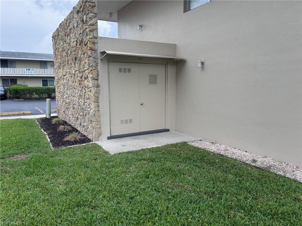 View of exterior entry with stucco siding, a lawn, and stone siding