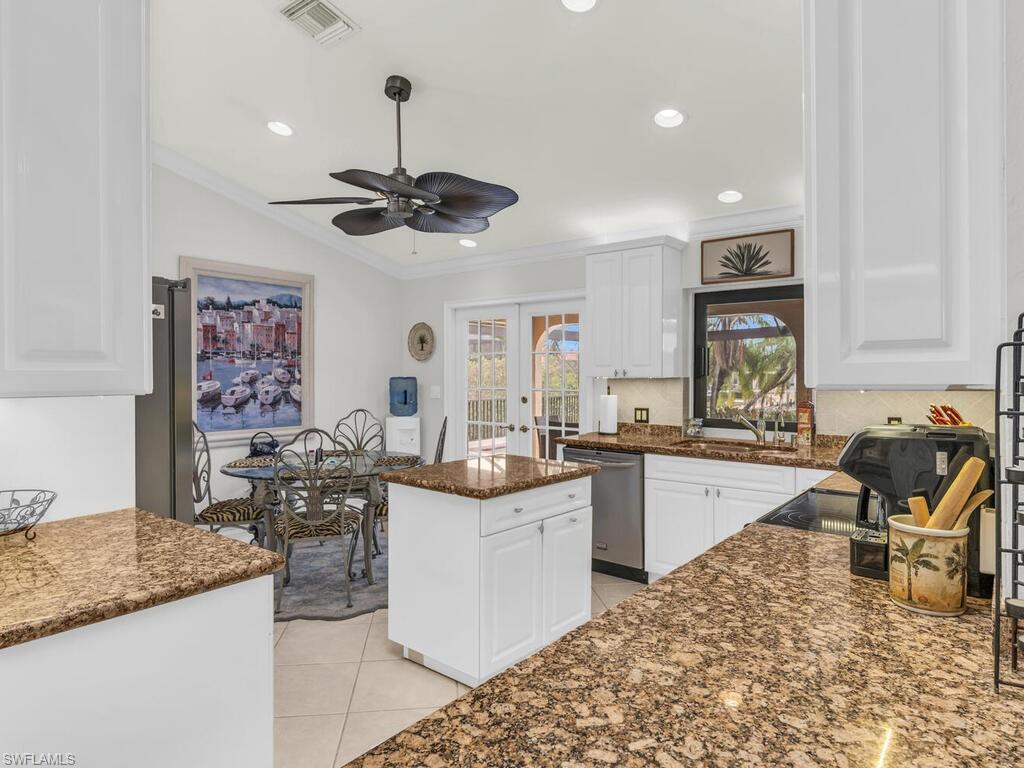 Kitchen featuring a center island, french doors, stainless steel dishwasher, light tile patterned flooring, and white cabinetry