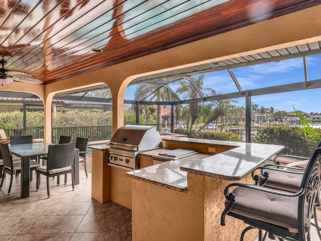 View of patio / terrace with glass enclosure, exterior bar, ceiling fan, a grill, and exterior kitchen