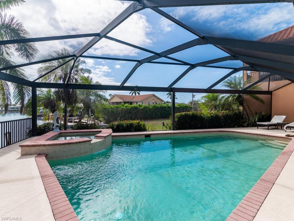 View of pool with glass enclosure, an in ground hot tub, a patio area, and a water view