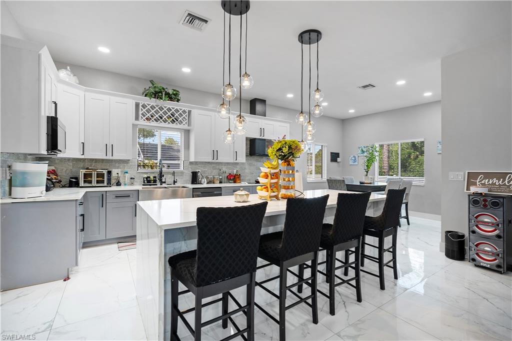 Kitchen featuring backsplash, light marble finish floors, light countertops, recessed lighting, and a kitchen bar