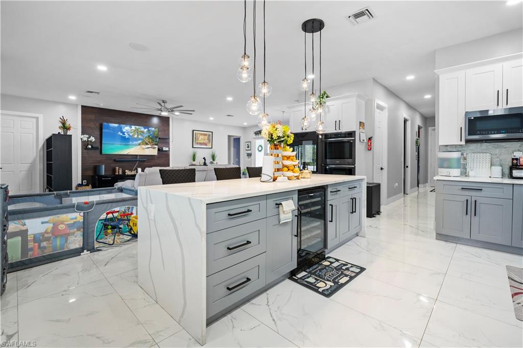 Kitchen with beverage cooler, stainless steel microwave, double oven, recessed lighting, and gray cabinetry