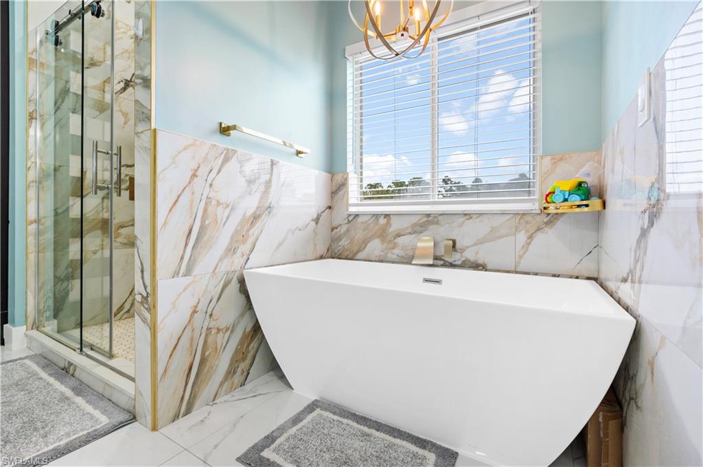 Full bathroom featuring tile walls, a chandelier, a marble finish shower, a freestanding bath, and marble tiled floors