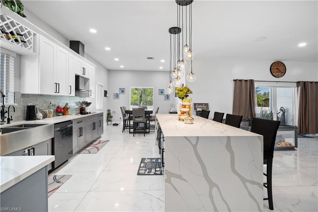 Kitchen featuring a kitchen breakfast bar, dishwashing machine, light stone counters, backsplash, and light marble finish floors