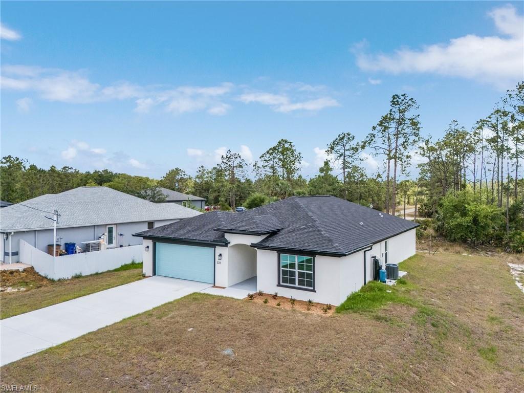 Ranch-style home with concrete driveway, an attached garage, a front yard, roof with shingles, and stucco siding