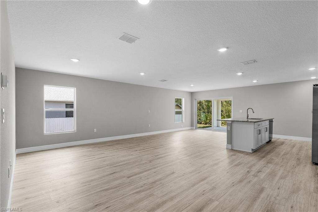 Unfurnished living room with a sink, light wood-type flooring, baseboards, recessed lighting, and a textured ceiling