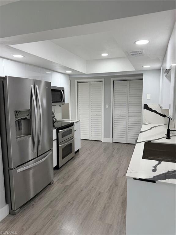 Kitchen with fridge, stove, white cabinetry, light wood-style flooring, and modern cabinets