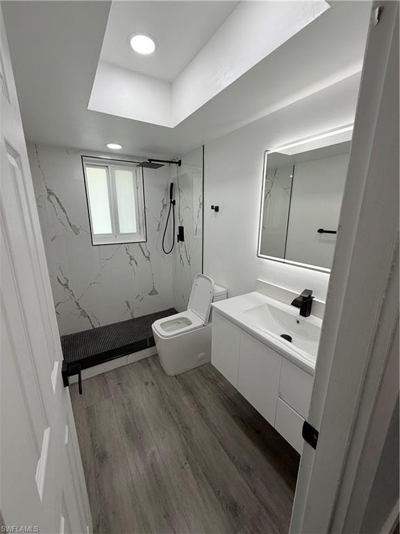 Bathroom featuring a marble finish shower, vanity, wood finished floors, and recessed lighting