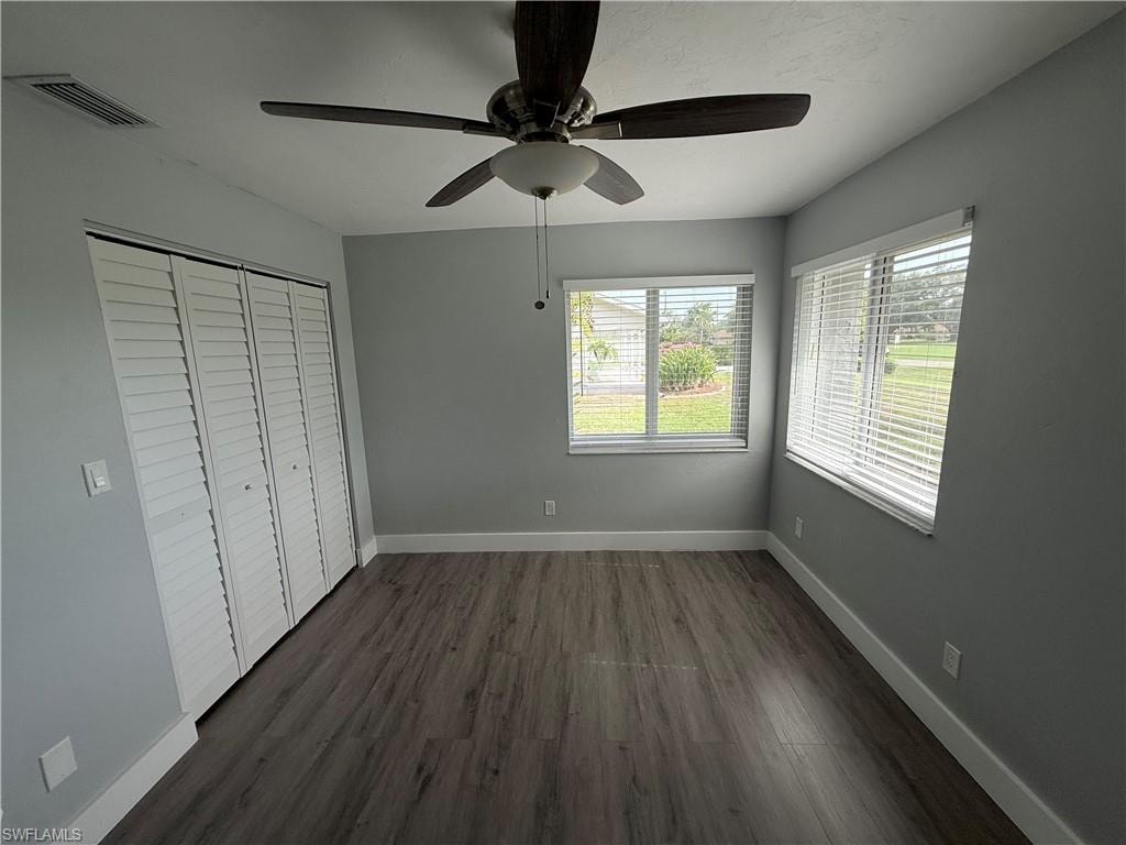 Unfurnished bedroom with multiple windows, dark wood-style flooring, a closet, and ceiling fan
