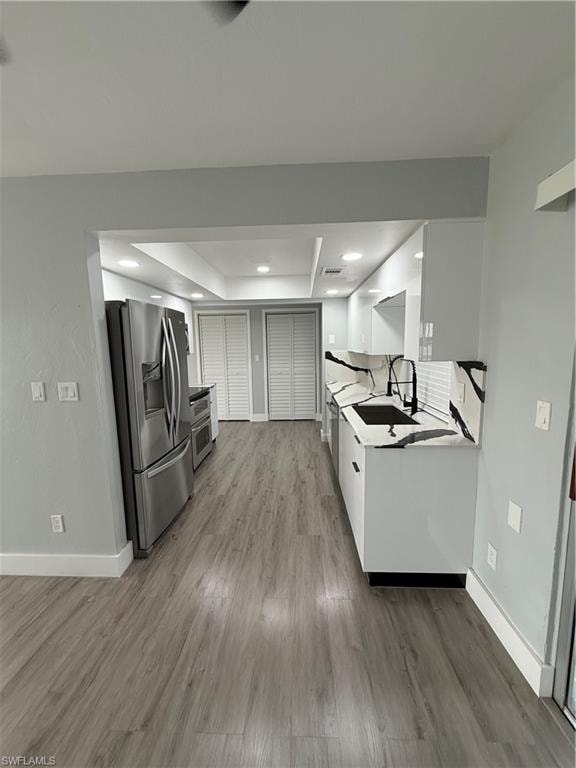 Kitchen with refrigerator, wood finished floors, a raised ceiling, light countertops, and recessed lighting