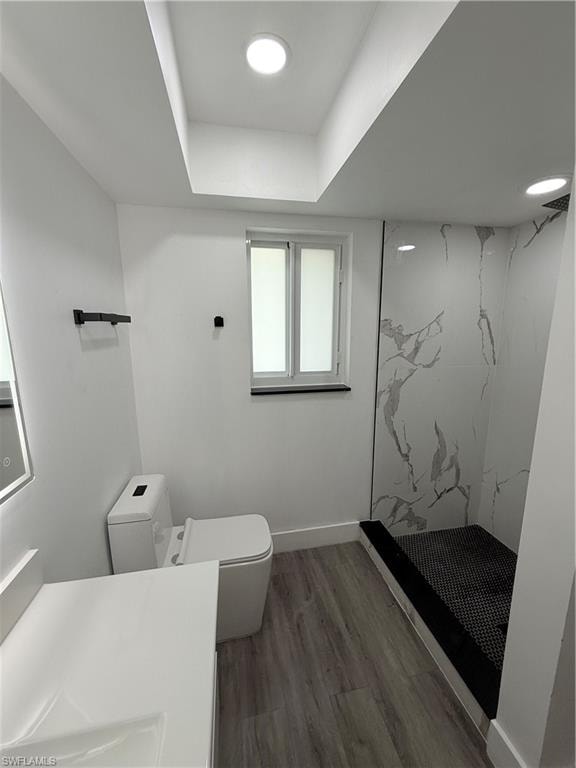 Bathroom featuring a marble finish shower, wood finished floors, vanity, and a tray ceiling
